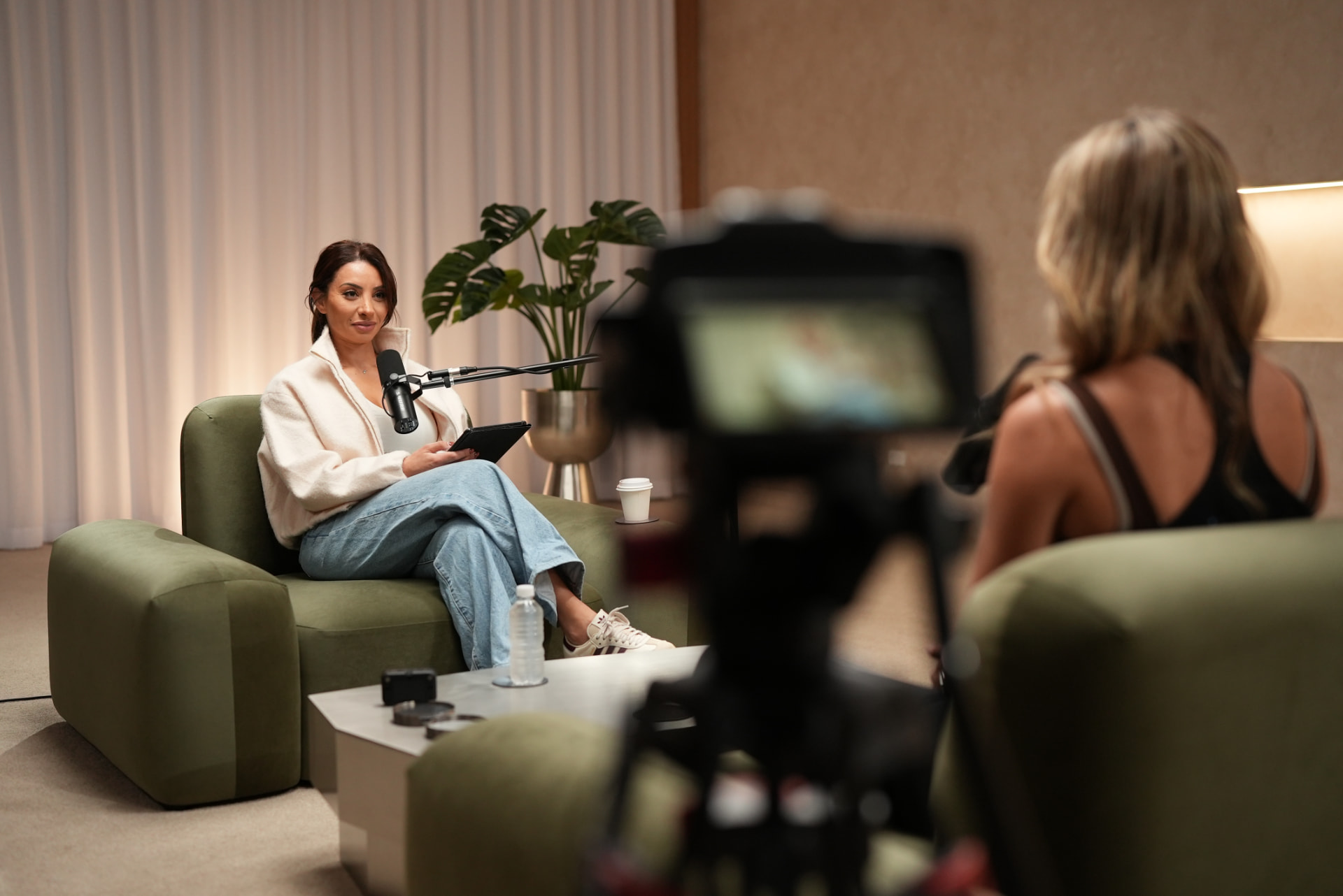 Host interviewing a guest on a green lounge set with warm curtain lighting